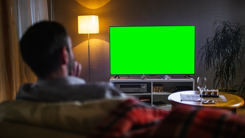 mann schaut auf einen fernseher mit gruenem bildschirm
