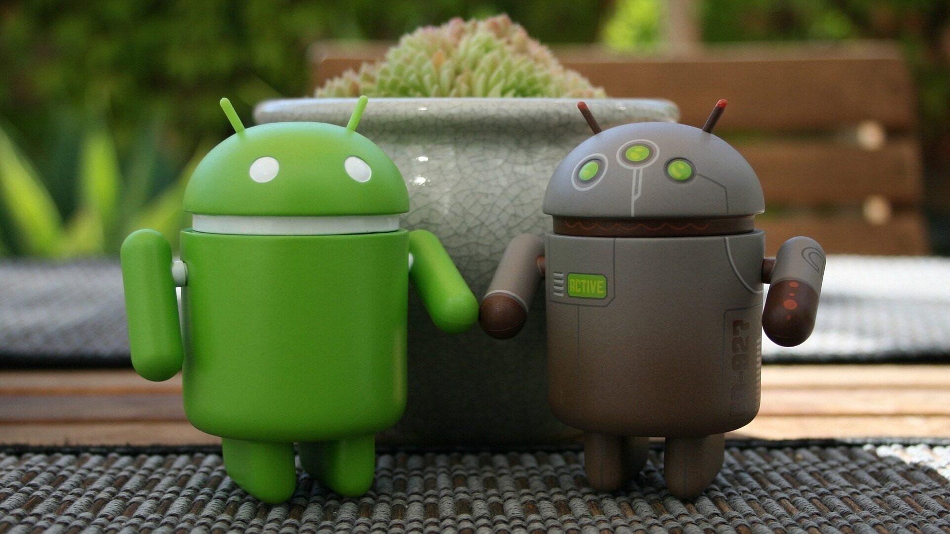zwei Android-Figuren vor einem Blumentopf